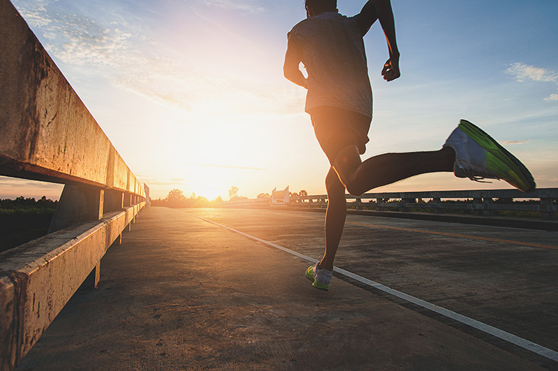 Man running along a road across a bridge at sunset